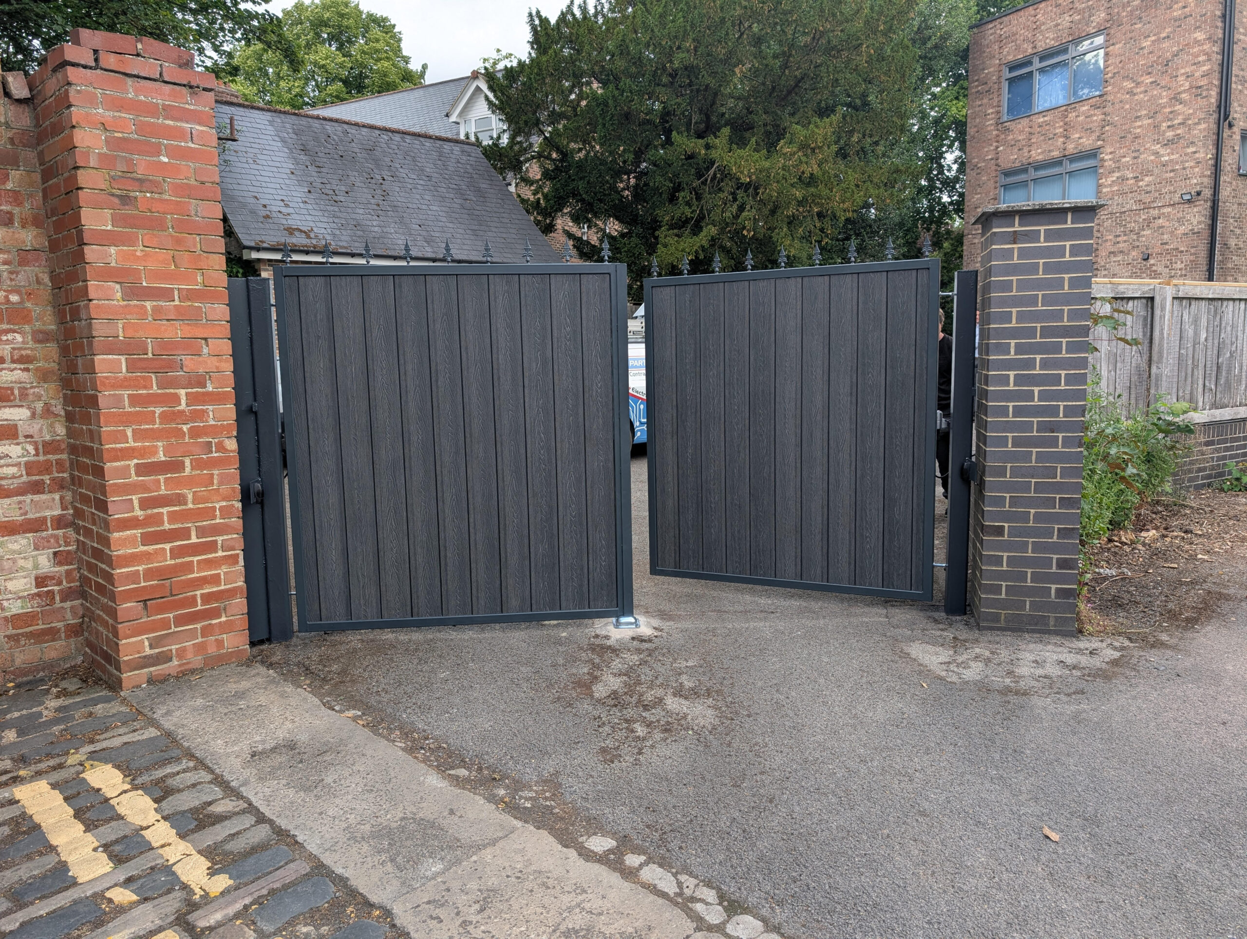 Grey automatic swing gates between brick pillars